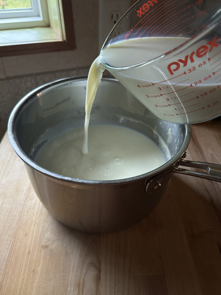 pouring raw milk with whey into pot on counter top