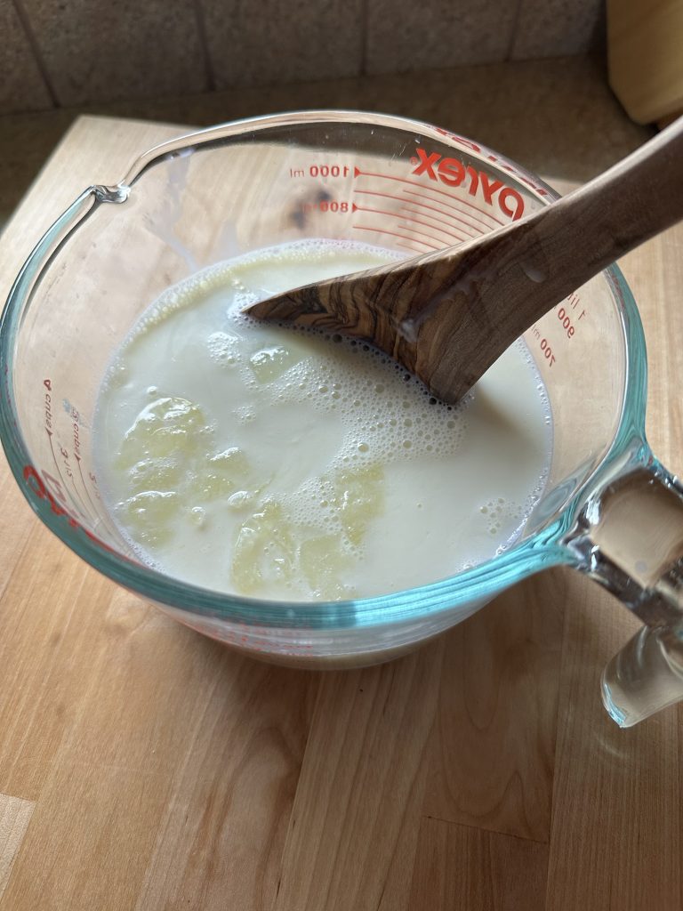 mixing frozen whey cubes into raw milk with wooden spon on counter