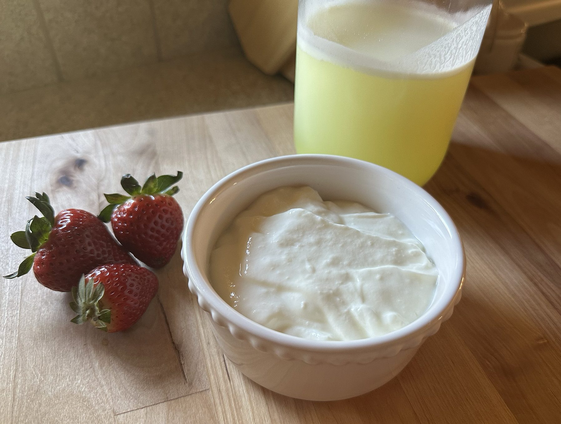 yogurt sitting in bowl next to strawberries and jar of whey