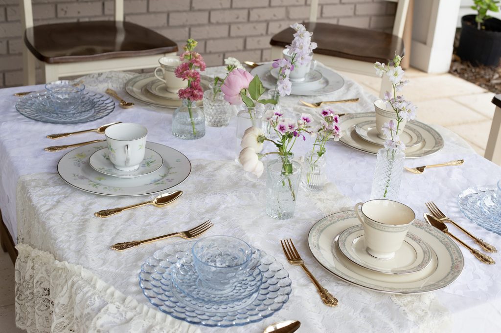 table with tea party place settings laid out on white table cloth with flowers on table for simple spring thrifted gems