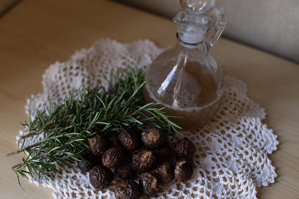 Homemade Soap Nut Shampoo sitting on table next to soap nuts and rosemary