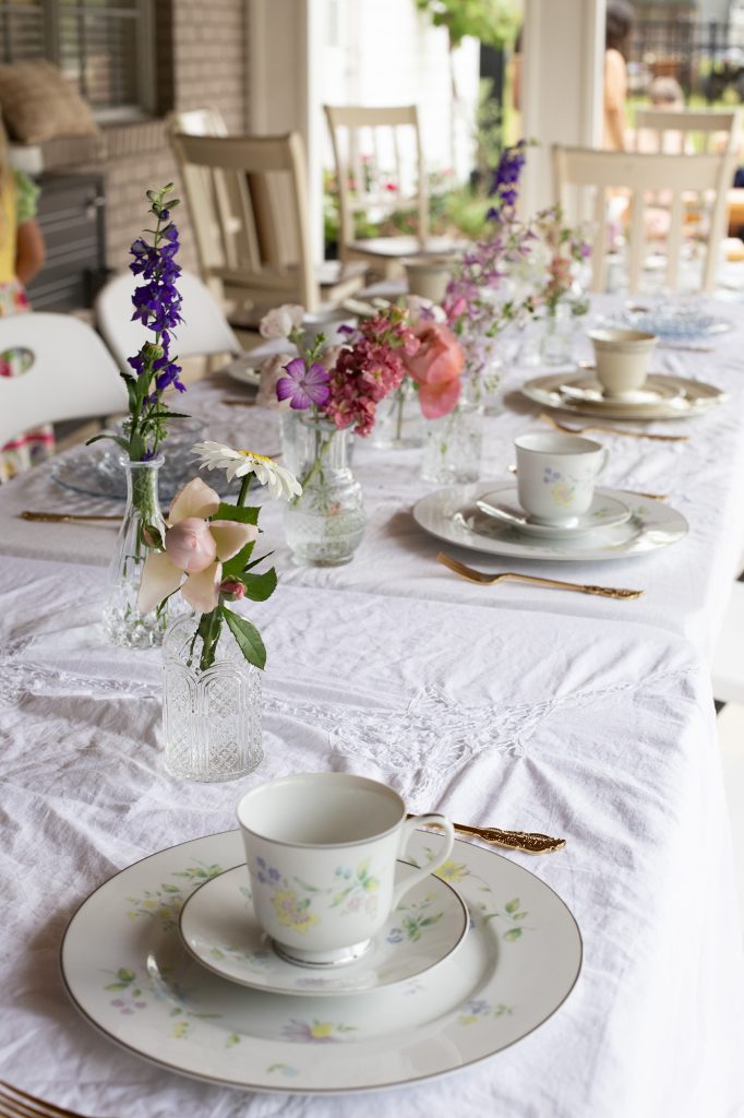 table with tea party place settings laid out on white table cloth with flowers on table for simple spring thrifted decor